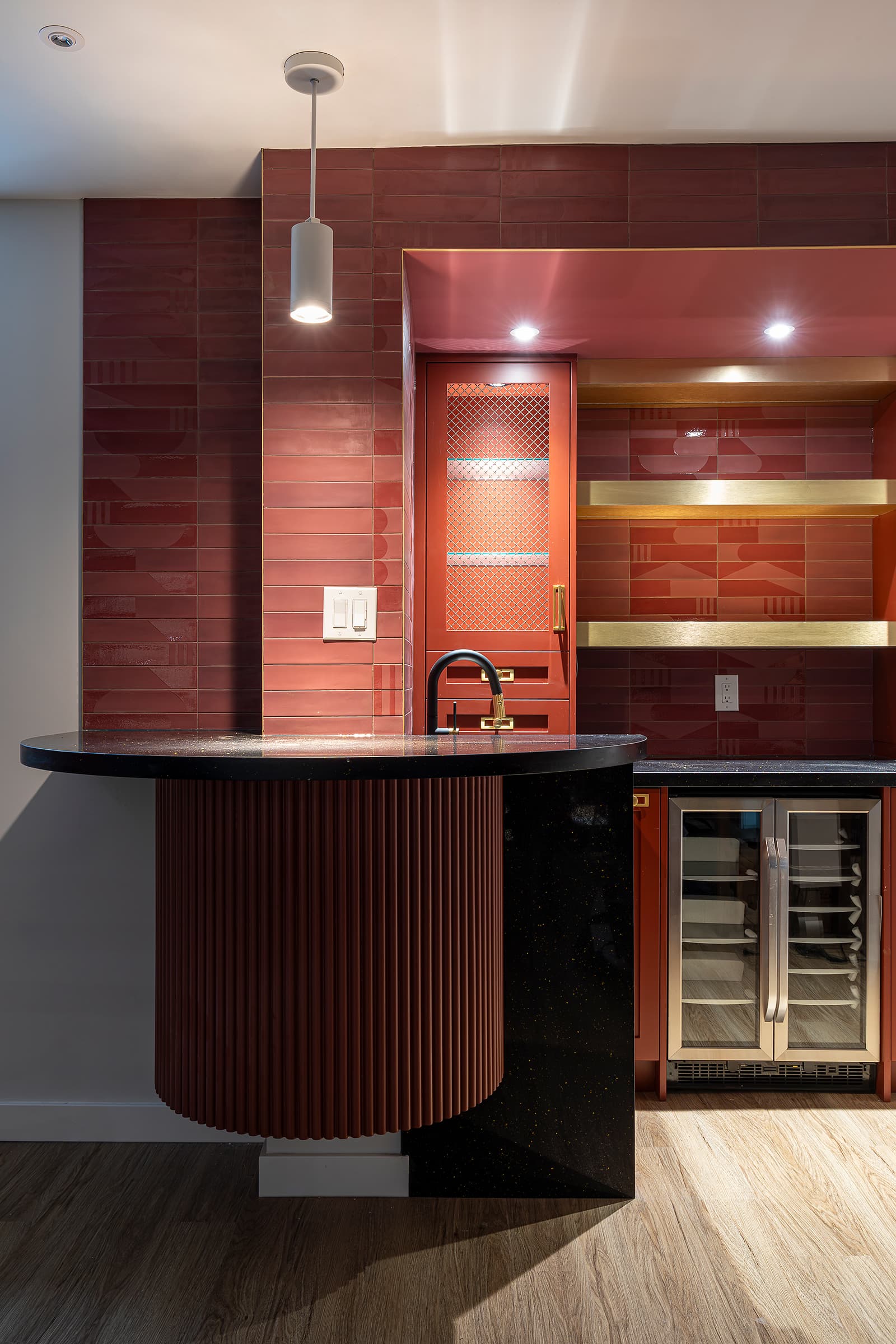 Modern home bar with burgundy fluted cabinetry, black quartz countertop, gold accents, and built-in wine fridge