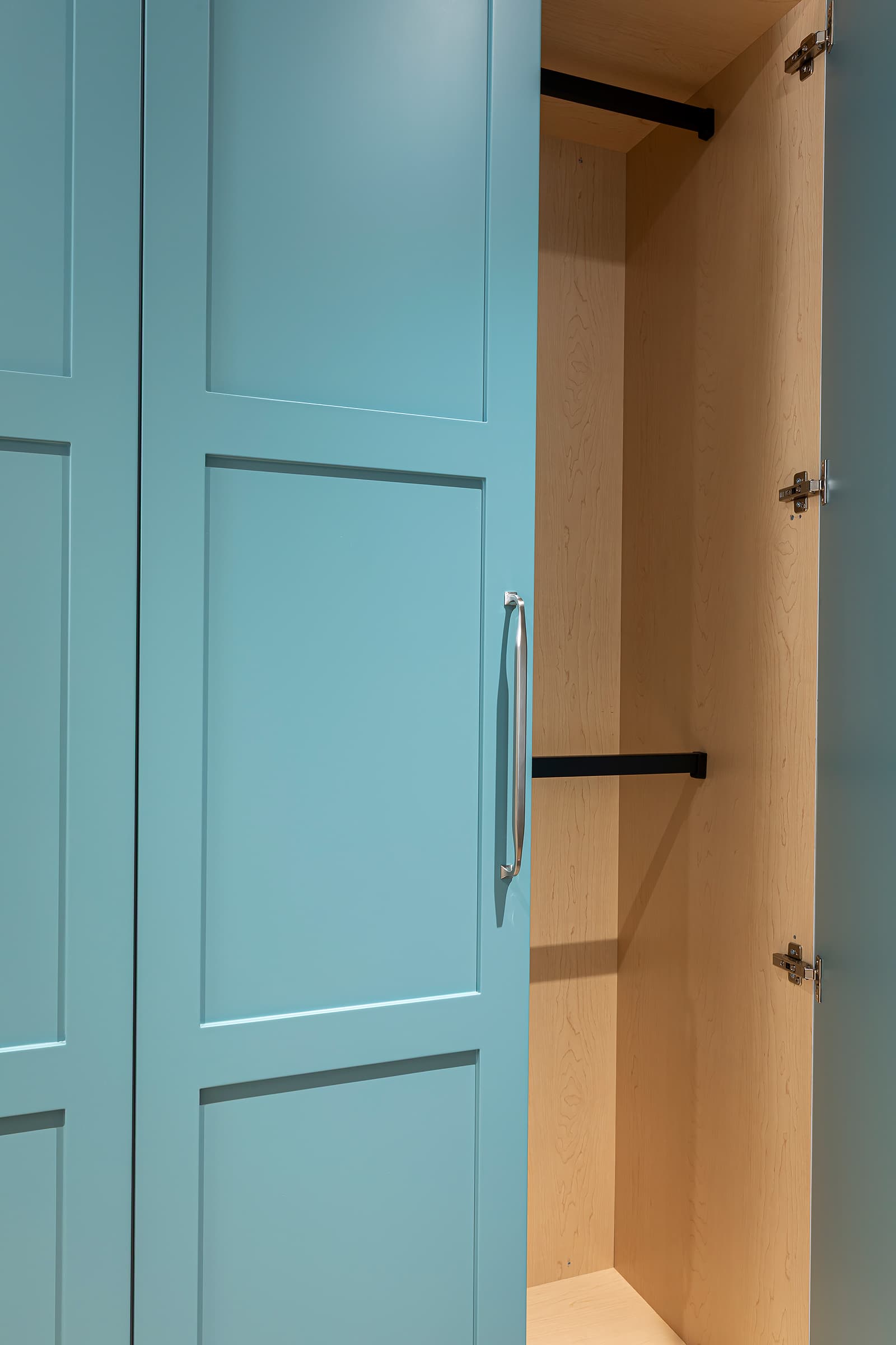 Partially open teal shaker-style hallway cabinet showing natural wood interior and black hanging rods