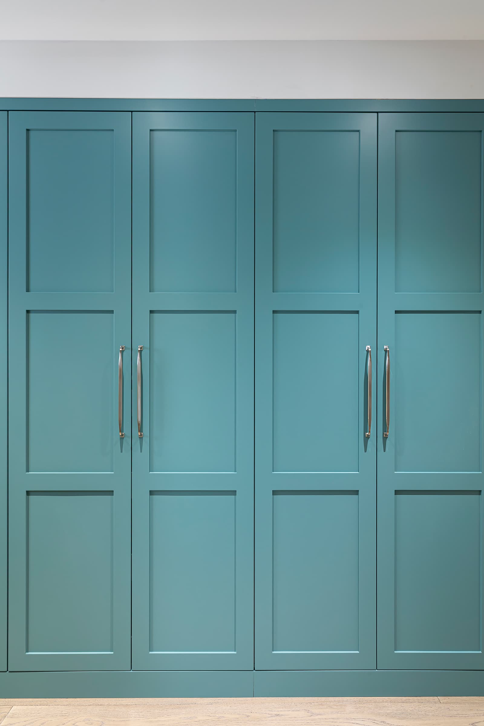 Built-in hallway closet with teal shaker-style cabinetry and brushed metal handles